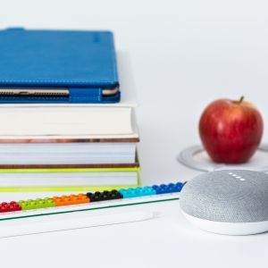 Drei Bücher auf einem Stapel mit einem Ipad oben drauf, ein Apfel, ein Lautsprecher, ein Lineal und ein Stift
